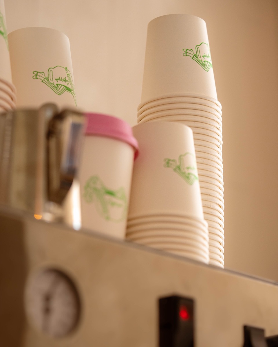 Branded Café Maud to-go cups stacked at the coffee window espresso machine