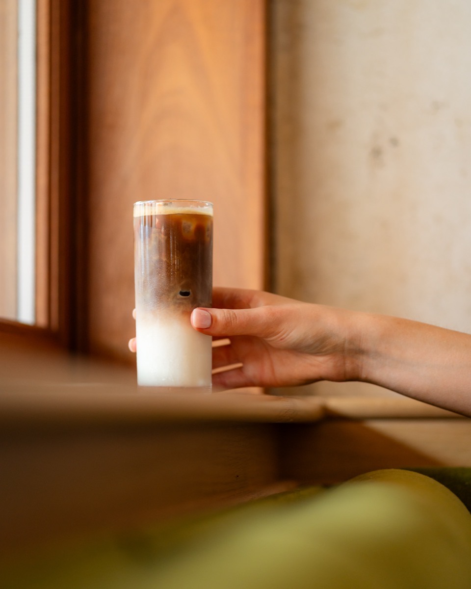 Hand holding a tall layered iced latte inside Café Maud