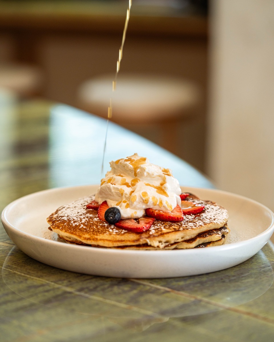 Stack of pancakes with strawberries, blueberries, and whipped cream — a Café Maud brunch favorite