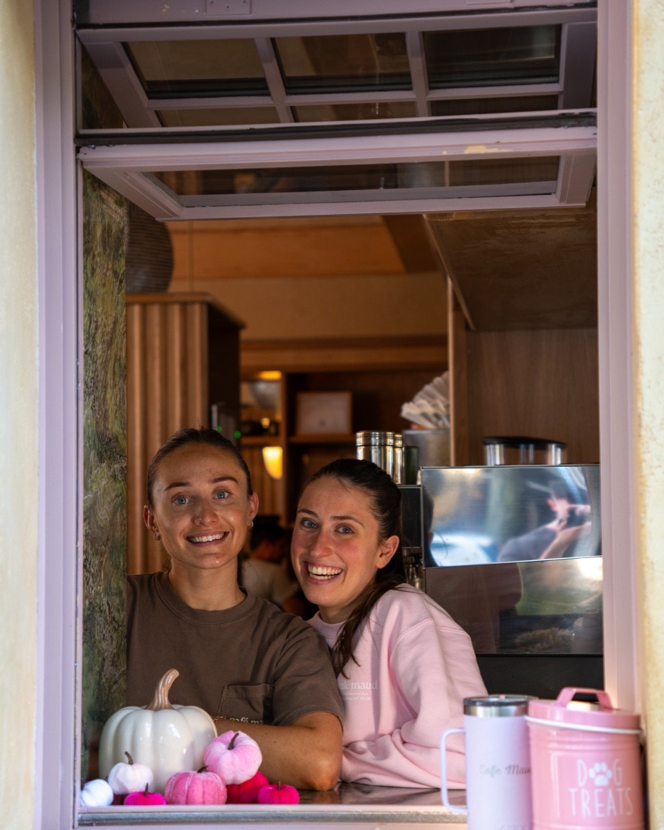 Two Café Maud team members smiling from the coffee window